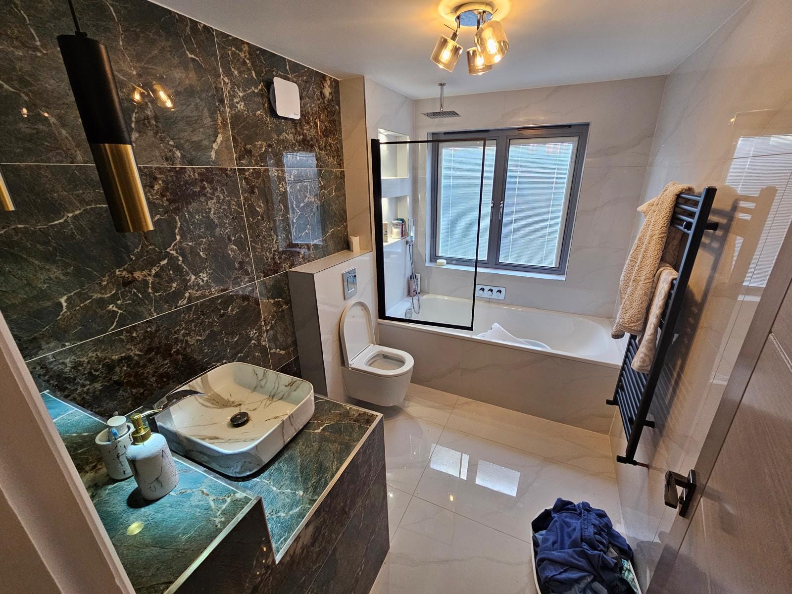 Finished bathroom with a wall-mounted extractor fan, a window over the bath, a heated towel rail and a basin on a tiled vanity.